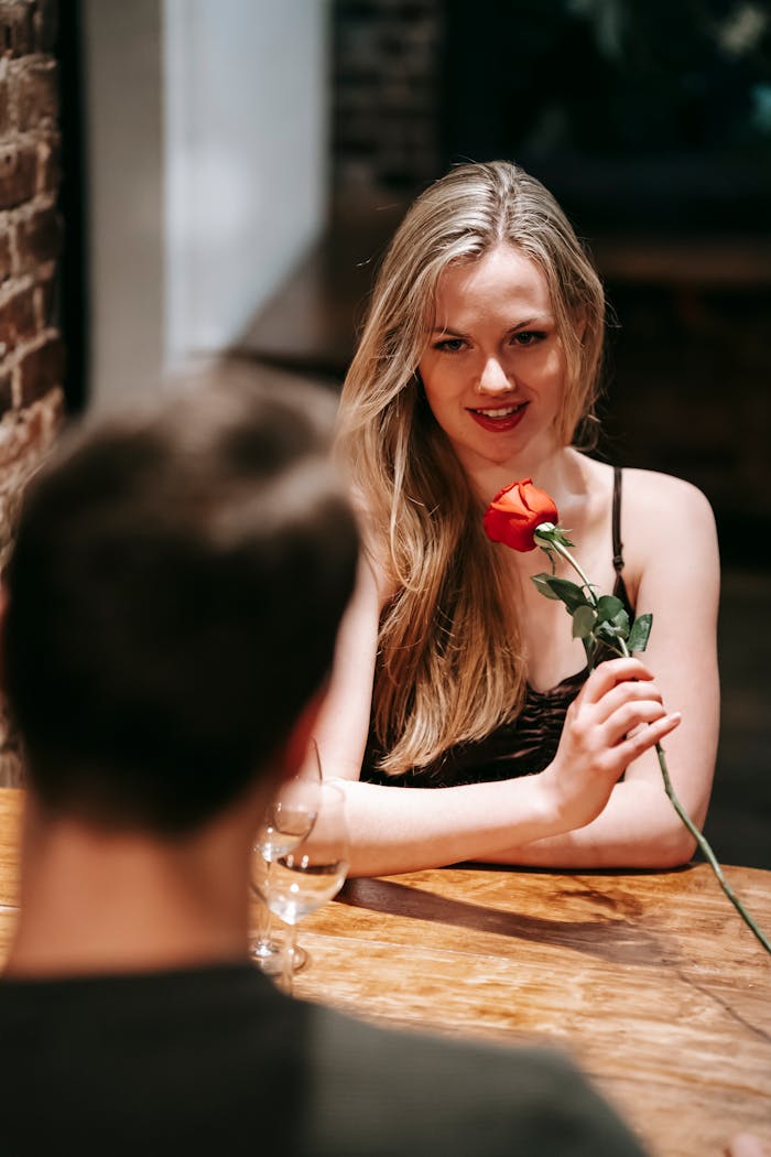 services-04 Young couple in elegant clothes sitting at table in light cafe while enjoying romantic dinner with wineglasses and red rose